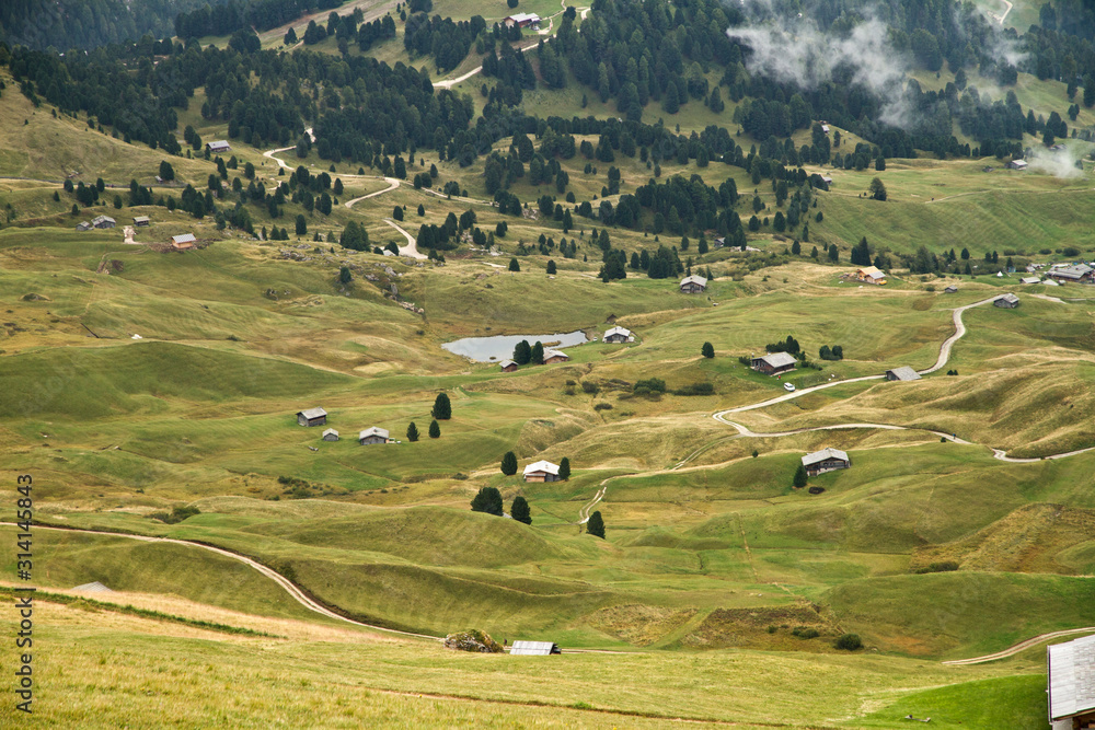 Hütten Wanderung auf der Almwiese der Alm im Herbst in den Dolomiten mit schöner Bergkulisse der Seceda im Grödner Tal in Südtirol Italien in Europa. Berghütten und Nebel und Wolken.