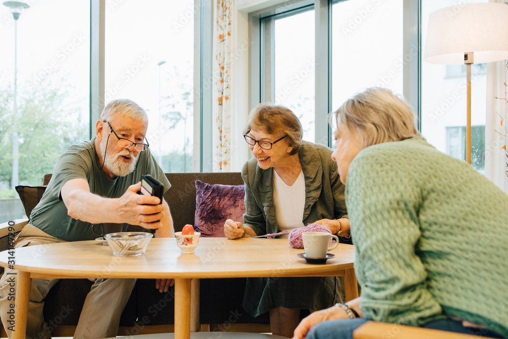 Retired elderly man sharing smart phone with friends sitting at table in nursing home Retired elderly man sharing smart phone with friends sitting at table in nursing home