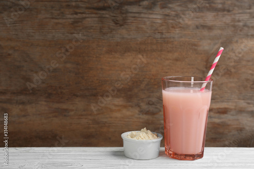 Protein shake and powder on white wooden table, space for text