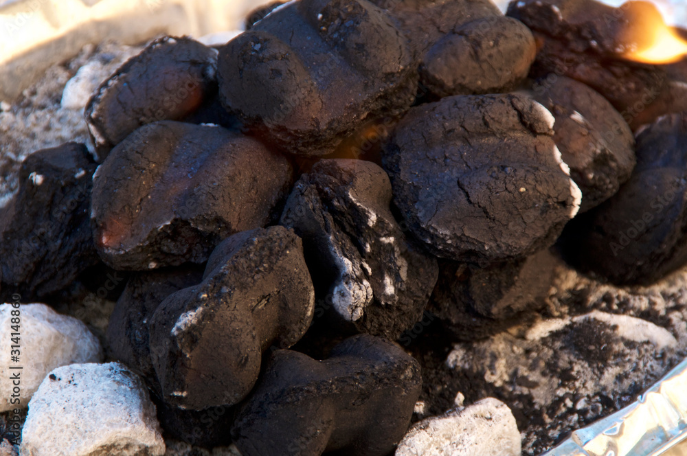 Close up of large stack of black charcoal barbecue briquettes with flame beginning to ash over. Close up of large stack of black charcoal barbecue briquettes with flame beginning to ash over.