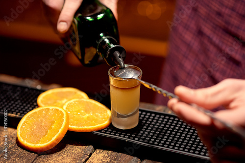 The bartender makes an alcoholic shot with an appetizer of orange sprinkled with cinnamon.