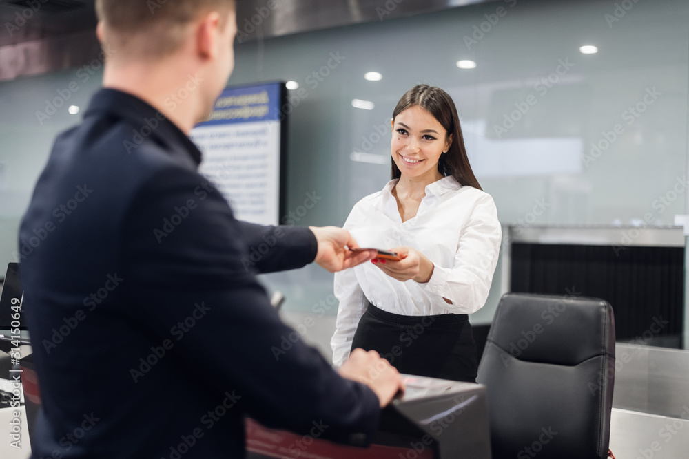 Business trip. Handsome young businessman in suit holding his passport and talking to woman at airline check in counter in the airport Business trip. Handsome young businessman in suit holding his passport and talking to woman at airline check in counter in the airport