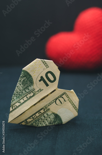 A heart made of paper money in the foreground and a red heart in the background, dark background. Romance and love concept