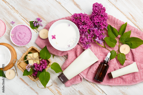 Spa and bath cosmetics with lilac flowers. Bath salt, soap, cream, oil, milk, serum and towel rolls on wooden rustic background. Organic natural cosmetic. Fresh care of body. Eco lifestyle