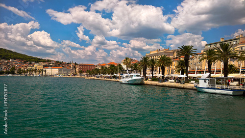 Seafront view at old city center in Split town. Romanesque buildings along sunny pier with palm trees.