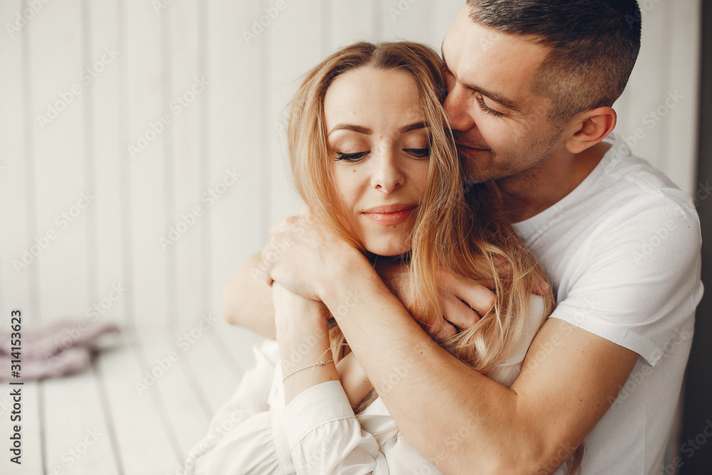 Couple sitting at home. Beautiful blonde with her husband. Man in a white shirt - obrazy, fototapety, plakaty 