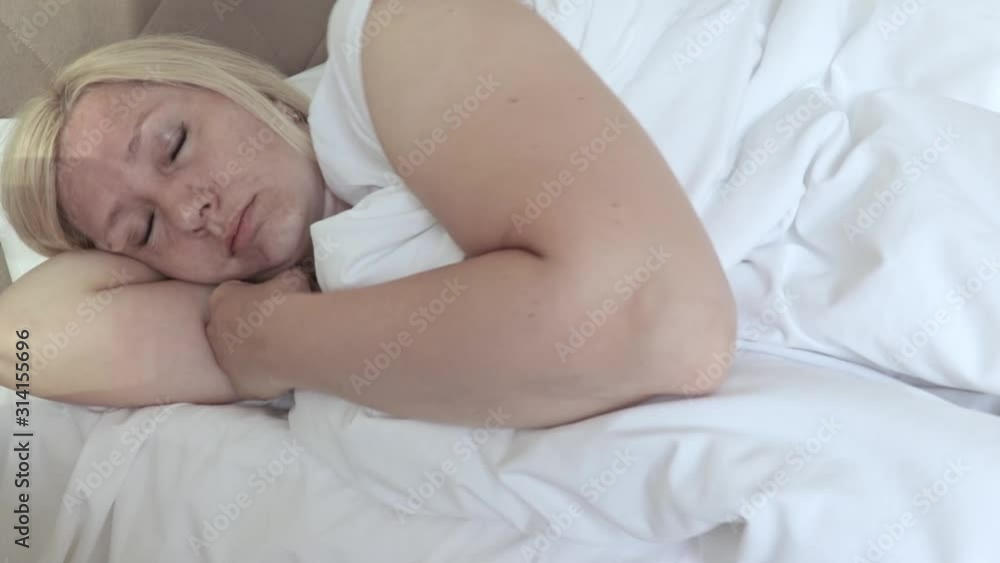 Sleepy middle aged woman lying in bed and trying to wake up by rubbing her eyes and face Sleepy middle aged woman lying in bed and trying to wake up by rubbing her eyes and face