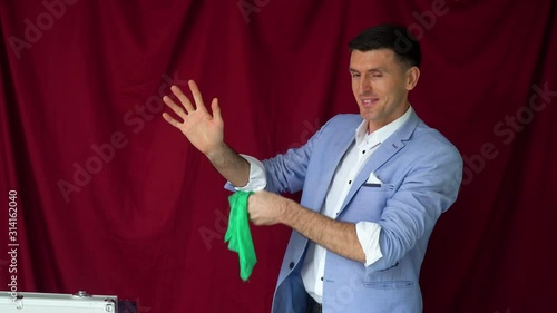 Magician in a suit shows a trick with shawl on a vinous background photo