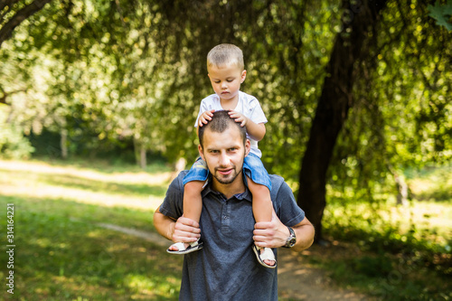 Cute little boy and his handsome young dad are looking forward and smiling while resting in the park. Son is sitting pickaback © F8  \ Suport Ukraine