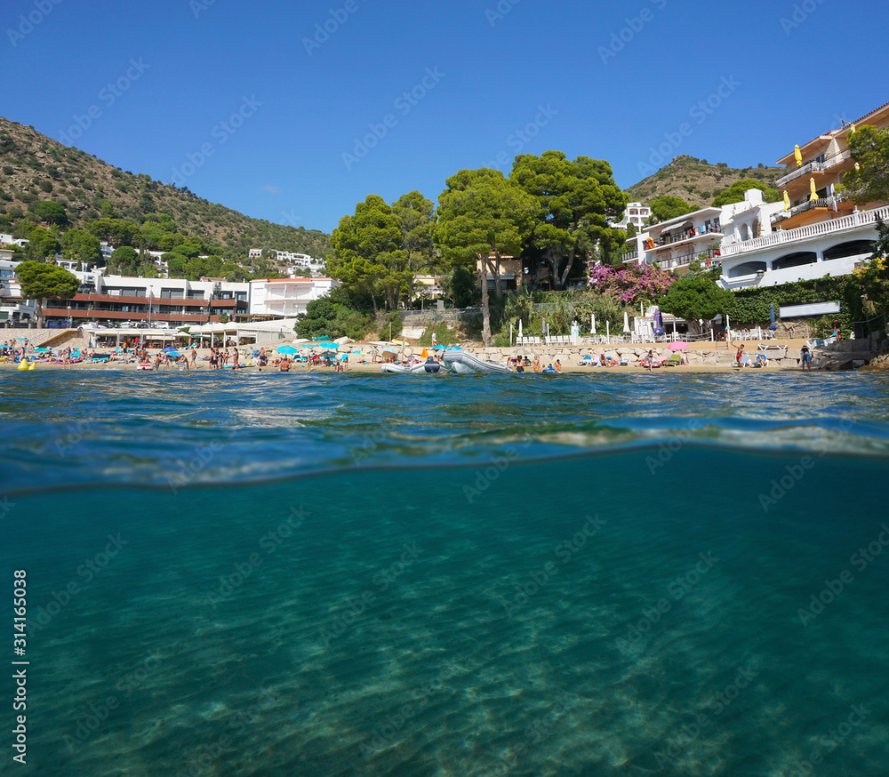 Mediterranean sea urban beach in summer in Spain on the Costa Brava with sand underwater, split view over and under water surface, Catalonia, Roses, Canyelles Petites