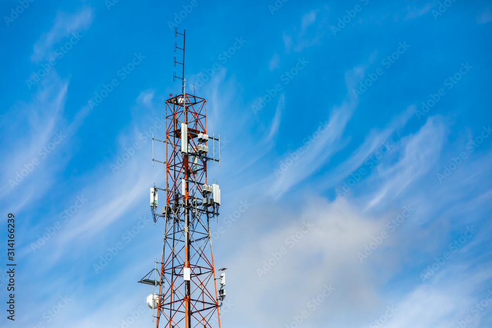 Wispy clouds are seen in the sky behind a tall pylon housing the infrastructure for mobile networks. Antenna send and receive data signals. With copy space
