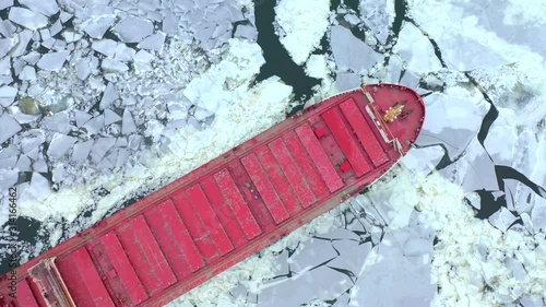 Big red freighter ship breaking through ice on the Great Lakes in winter, aerial view.