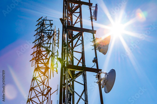 Bright sun shine over two cell site towers, radio and GPS transmitter and receiv Fototapet