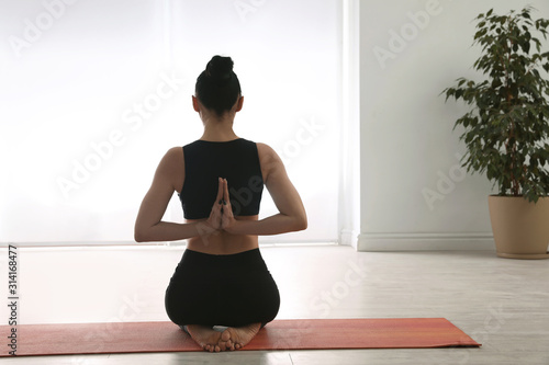 Woman practicing vajrasana with namaste behind back in yoga studio