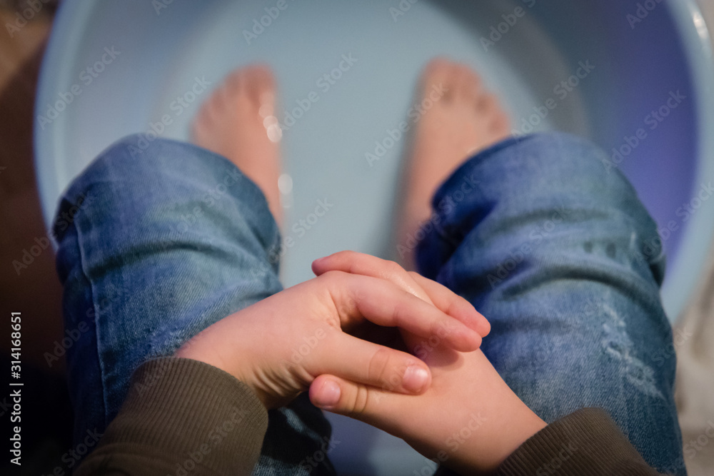 A boy relaxing at home and worming his feet in hot salt water in the plastic wash bowl. A boy relaxing at home and worming his feet in hot salt water in the plastic wash bowl.