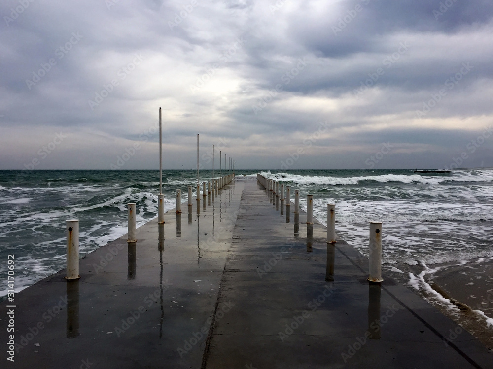 Cloudy weather, waves, sea and pier in the center. Sea with waves in cloudy weather.