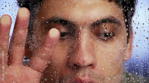 guy Caucasian appearance looks through a wet window after a rain. Close-up.