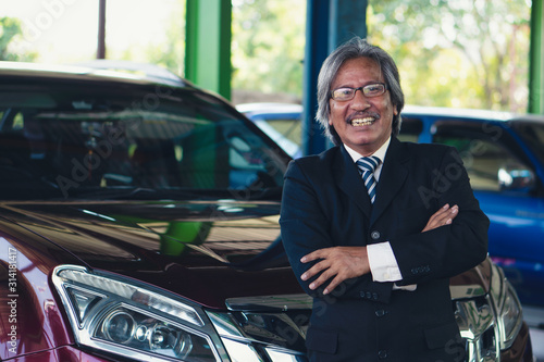 portrait of happy elder customer with his car at garage and car maintenance service station