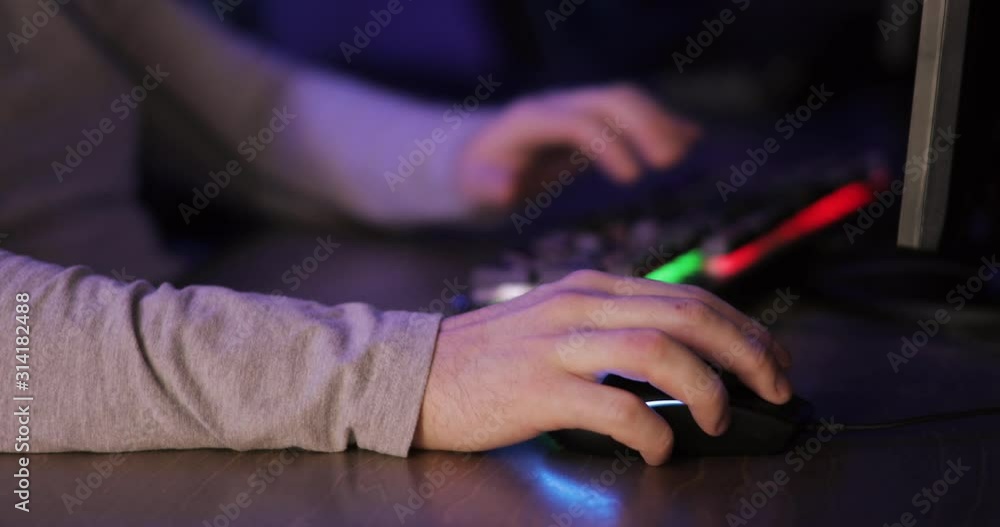 Man gamer is playing computer game sitting at table, hands closeup. Hands of gamer pressing a key on keyboard and mouse in dark. Concept of dependence on computer games and relaxing. Man gamer is playing computer game sitting at table, hands closeup. Hands of gamer pressing a key on keyboard and mouse in dark. Concept of dependence on computer games and relaxing.