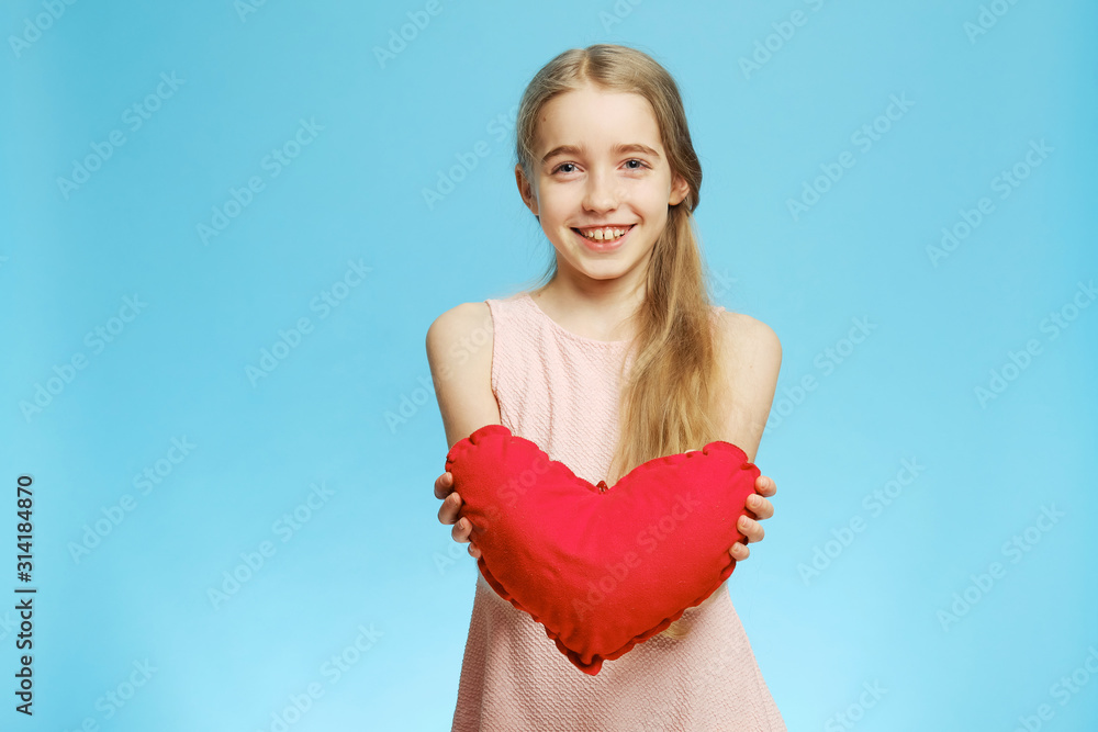 Cheerful little girl with a heart made of cloth on a blue background. Isolated half-length portrait. Cheerful little girl with a heart made of cloth on a blue background. Isolated half-length portrait.