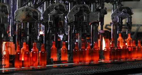 Automated conveyor mashinery line for production of glass bottles in plant. Manufacturing industrial modern factory. Robotic machine puts hot glowing glass bottles on conveyor lo move it.