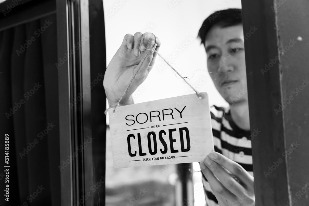 through-glass-view-of-asian-male-business-owner-hanging-up-sign-with