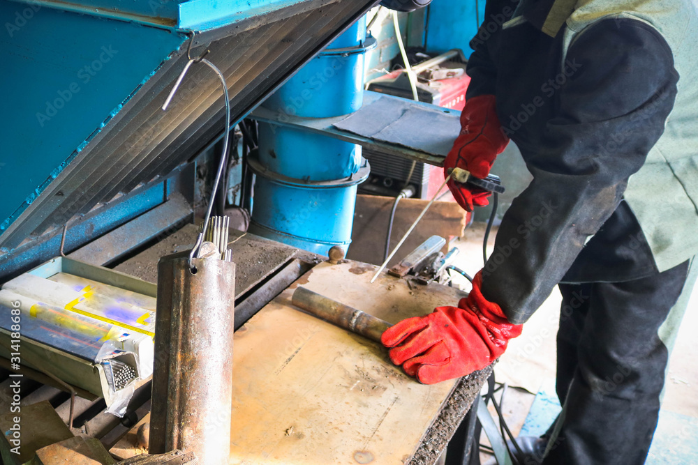 A male worker, a welder in professional work clothes, works on a welding table for the repair and manufacture of parts and spare parts A male worker, a welder in professional work clothes, works on a welding table for the repair and manufacture of parts and spare parts