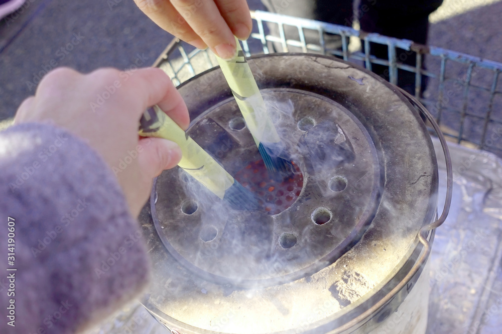 Fototapeta premium Close up of elder hands holding Japanese joss sticks which is being lighted up in a stove with smoke at Sensoji Temple also know as Asakusa temple located in Tokyo, Japan