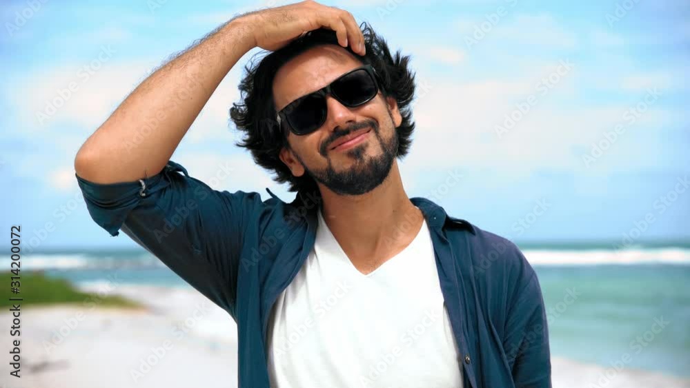 Portrait of a young handsome man with a beard in sunglasses on the background of the tropical beach and a blue sea. Portrait of a young handsome man with a beard in sunglasses on the background of the tropical beach and a blue sea.