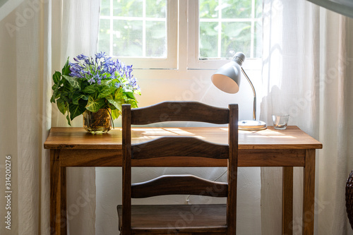 Wooden table with chair  lamp and a bouquet of flowers near the window in modern working area at home