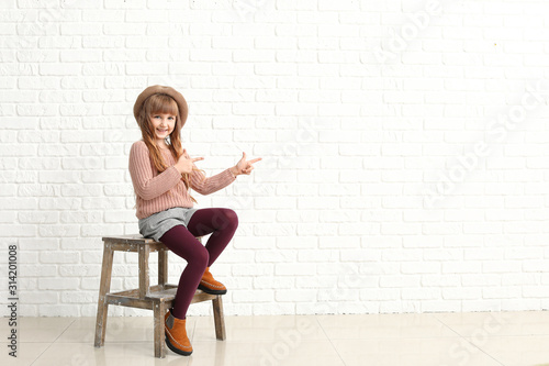 Cute fashionable girl showing something near white brick wall