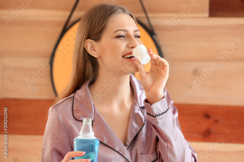 Beautiful young woman with mouth rinse in bathroom