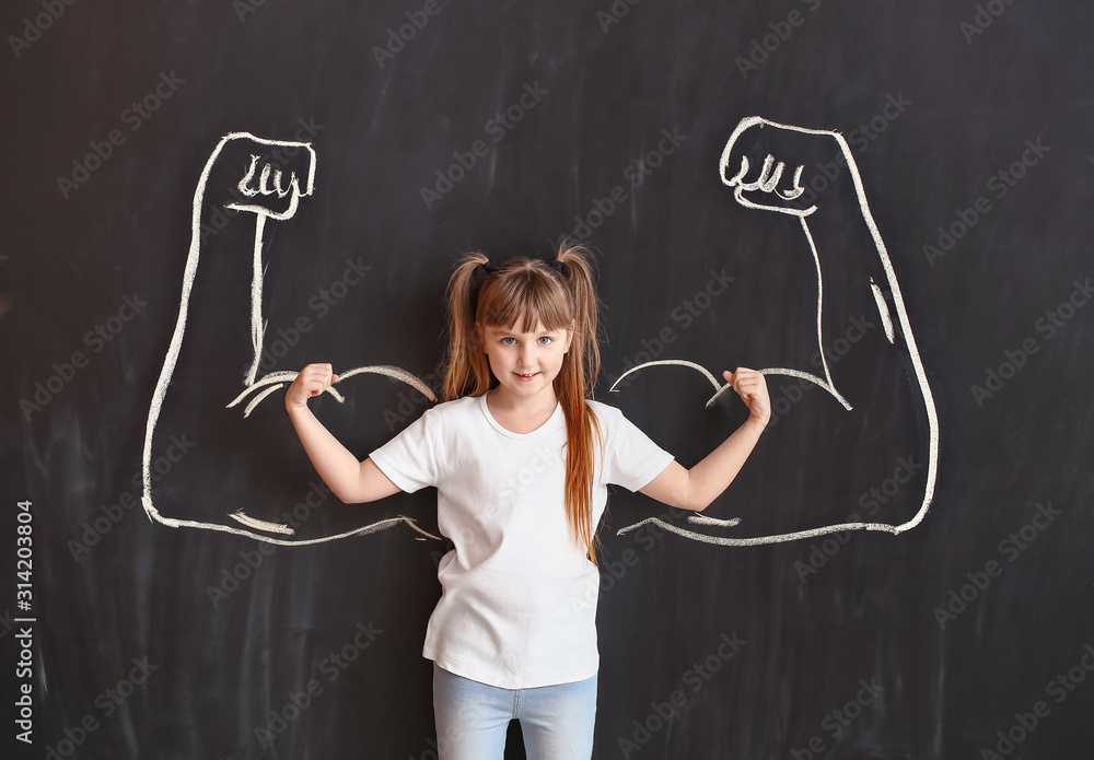 Little girl near dark wall with drawn muscular arms. Concept of feminism