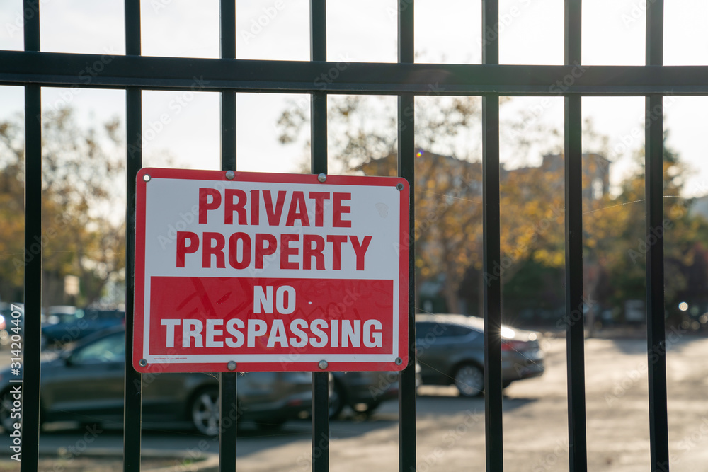 Private property no trespassing sign on black gate in front of parking lot Private property no trespassing sign on black gate in front of parking lot