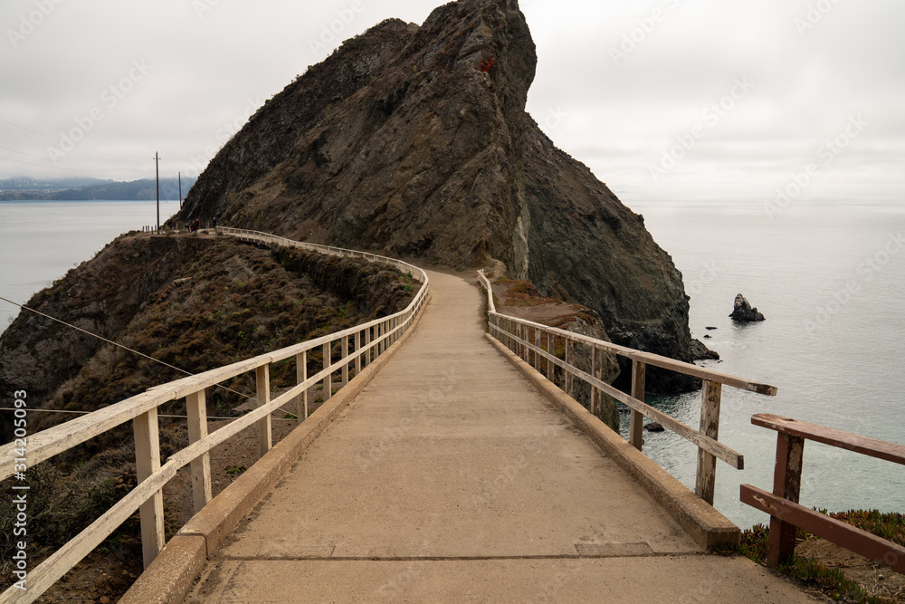 Concrete foot bridge with white wooden handrails leading to a cliff above sea