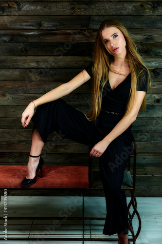 The model sits in various poses in front of the camera on a stand. The concept of fashion and style. Portrait of a pretty blonde girl with long hair and great makeup on a wooden background.