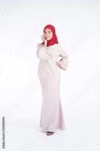 Attractive Muslim female model wearing a cream colored modern kebaya with red hijab, an Asian Muslim traditional dress isolated on white background. Eidul fitri fashion and lifestyle portrait concept.
