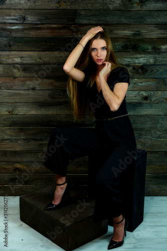 The concept of glamor, style. The model sits in different poses on an alternative stand in front of the camera. Portrait of a pretty blonde girl with long hair and great makeup on a wooden background.