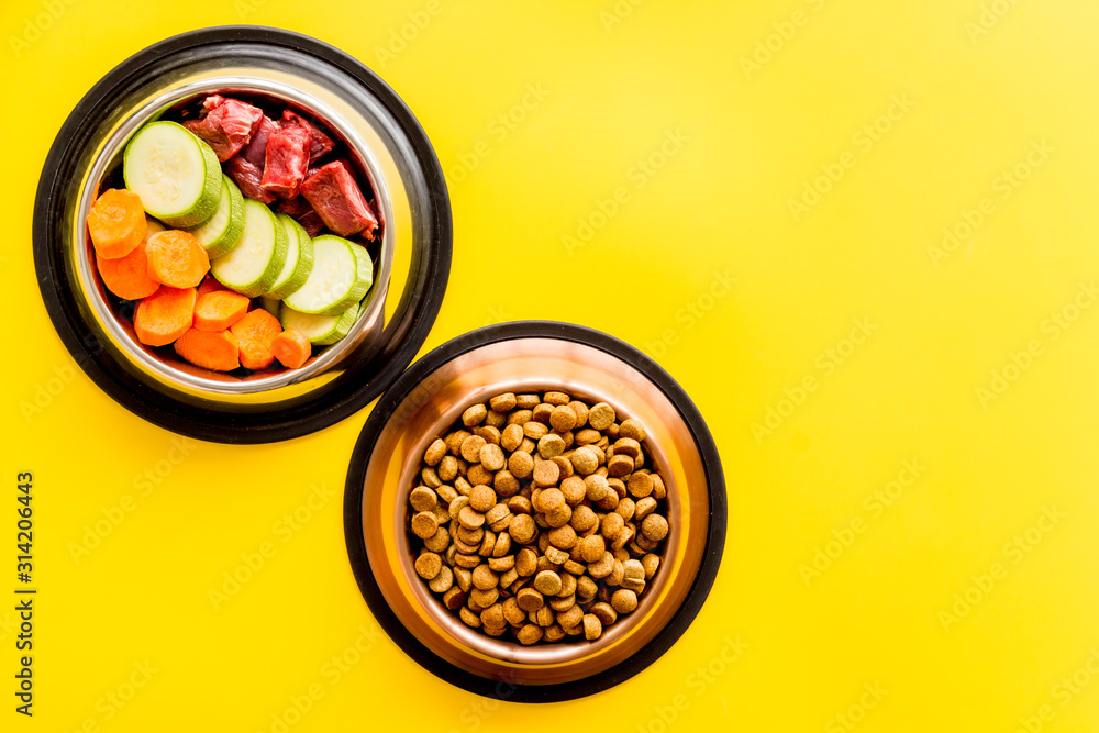 Healthy feed for cats and dogs. Bowls full of dry feed, meat and vegetables on yellow background top-down copy space Healthy feed for cats and dogs. Bowls full of dry feed, meat and vegetables on yellow background top-down copy space