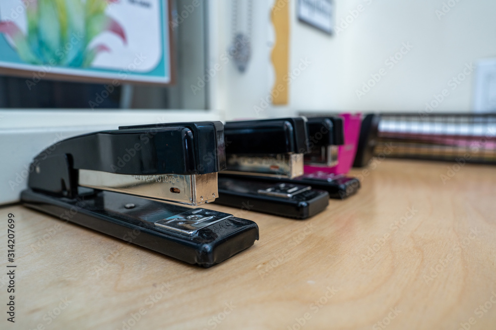 Row of black staplers and tape dispensers sitting on table in office environment Row of black staplers and tape dispensers sitting on table in office environment