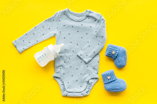 Cute baby clothes - suit - booties and accessories on yellow table top-down