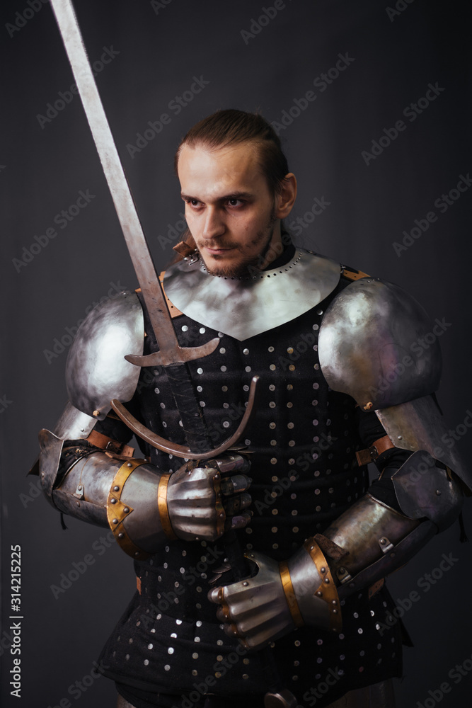 Naklejka premium Portrait of a medieval knight with a two-handed sword. Warrior in the studio on a dark background.