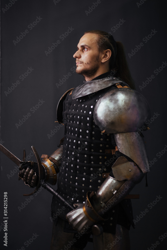 Naklejka premium Portrait of a medieval knight with a two-handed sword. Warrior in the studio on a dark background.