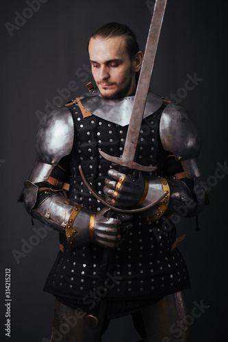 Portrait of a medieval knight with a two-handed sword. Warrior in the studio on a dark background.