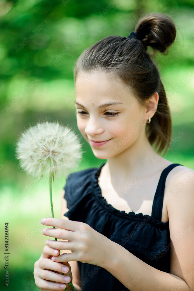Summer outdoor portrait of a romantic girl with a big fluffy dandelion. the child holds a dry dandelion in his hands. soft focus. Summer outdoor portrait of a romantic girl with a big fluffy dandelion. the child holds a dry dandelion in his hands. soft focus.
