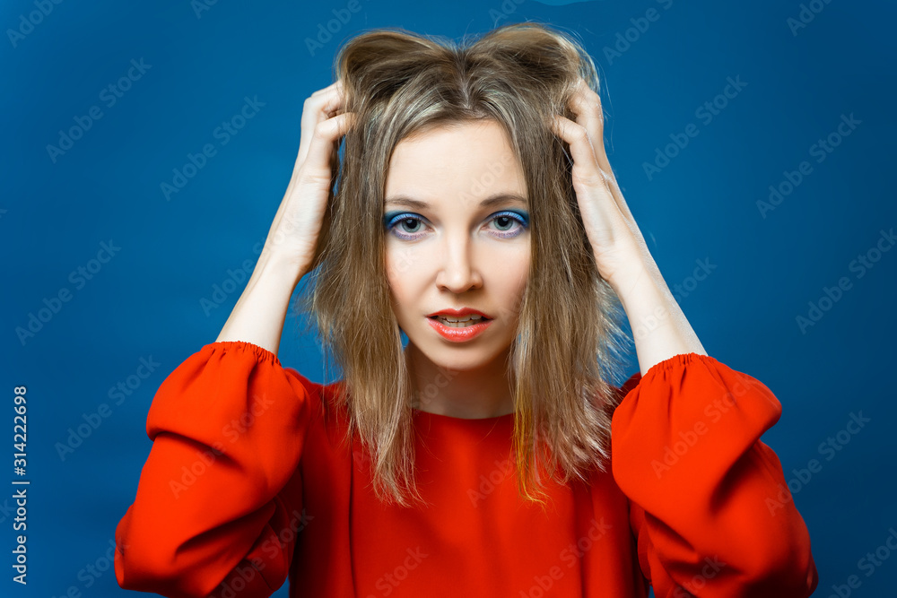 Beautiful young girl in red dress on blue background. Surprised, late for a meeting, desperate, panicked. Hands on head mouth wide open Beautiful young girl in red dress on blue background. Surprised, late for a meeting, desperate, panicked. Hands on head mouth wide open