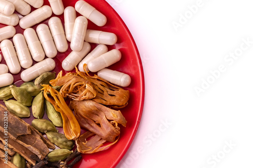Ancient Indian medicine system called Ayurveda and its present place in healthcare concept. Assorted spices with herbal capsules in a red dish on white background photo