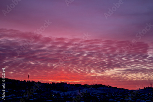 Pink dawn over a small town. City silhouette with a beautiful sunset. Dark winter landscape  outlines of mountain and forest against a background of pink  feather-like clouds. Artistically blurry.