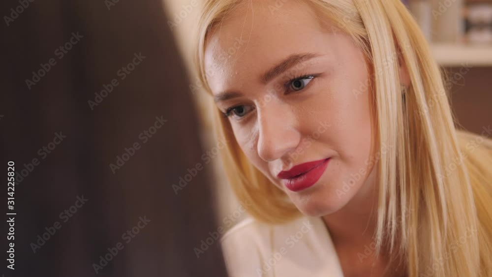 Portrait of a young female makeup artist with long blonde hair and red lipstick in a beauty salon while working with a client. Portrait of a young female makeup artist with long blonde hair and red lipstick in a beauty salon while working with a client.