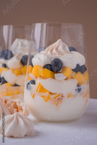 Eton mess - whipped cream, meringue, fresh blueberries and mango in glasses on a light table. Traditional English dessert. 